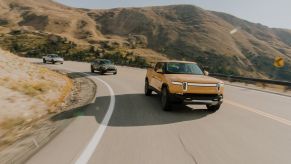 Three Rivian R1T models driving along a curved road by a cliff. The 2024 Rivian R1T is becoming a contender.