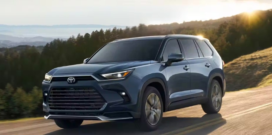 A blue 2024 Toyota Grand Highlander midsize three-row SUV is driving on the road. 