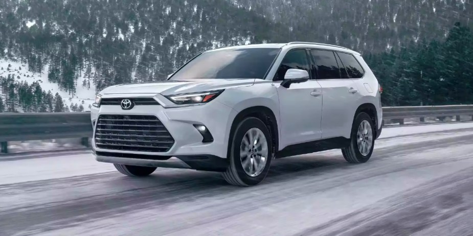 A white 2024 Toyota Grand Highlander midsize three-row SUV is driving on a snowy road. 