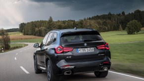 The rear of a black BMW X3 driving on a stormy road. The BMW X3's price isn't that bad compared to others in the class.