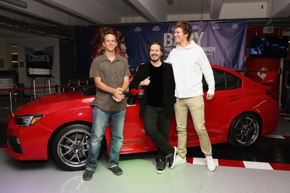 Three men stand in front of the bright red Subaru which starred in Baby Driver the movie.