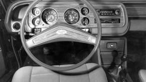 A black and white photo of a Ford Granada interior featuring its steering wheel, dashboard, and transmission