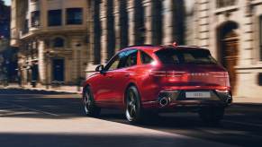 A red 2023 Genesis GV70 driving down a city road. The Genesis GV70's price is a big positive point.