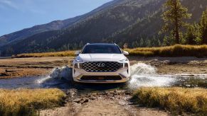 A white 2023 Hyundai Santa Fe midsize SUV is driving through the water.