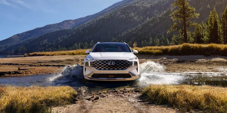 A white 2023 Hyundai Santa Fe midsize SUV is driving through the water.