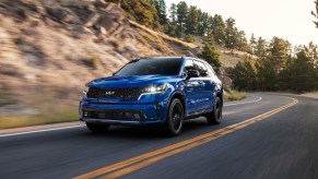 A blue 2023 Kia Sorento driving next to a hill. This Kia 3-row SUV is still a premium option.