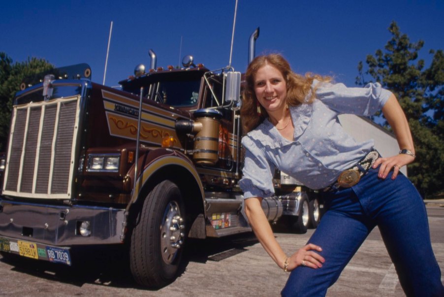 A female truck driver from Nebraska stands next to her big rig parked in California.