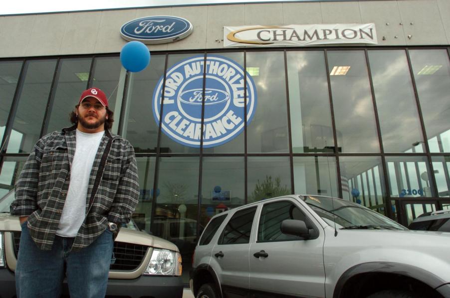 A man standing in front of a new car dealership in the 1990s.