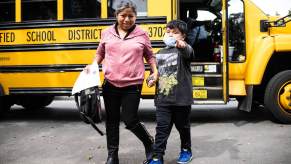 A little boy points while his mother leads him away from a school bus stop.