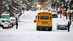 Parents watch students get on a school bus parked on a snowy street.