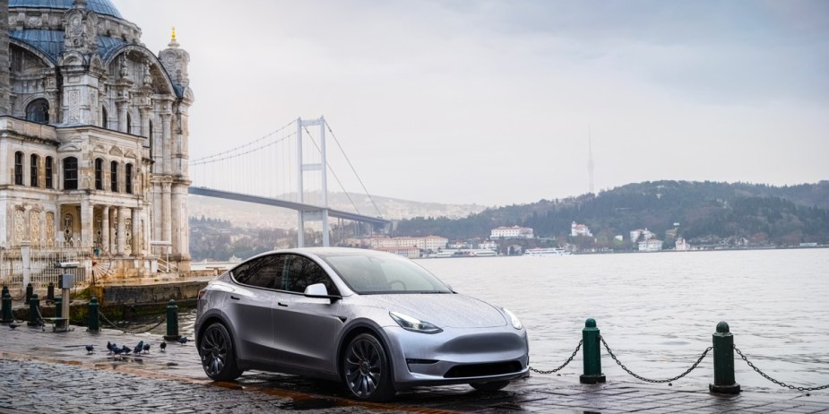 A gray 2023 Tesla Model Y small electric SUV is parked near water. 