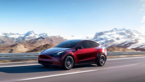 A red 2023 Tesla Model Y small electric SUV is driving on the road.