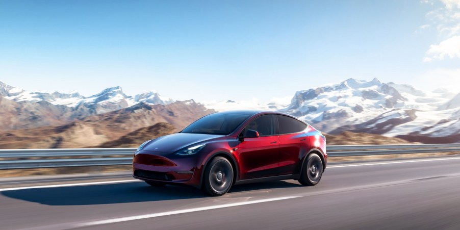 A red 2023 Tesla Model Y small electric SUV is driving on the road.