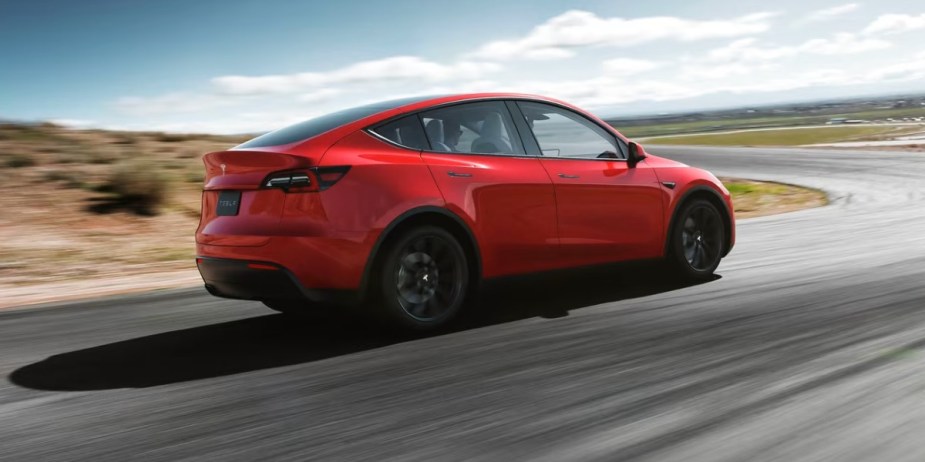 A red 2023 Tesla Model Y small electric SUV is driving on the road. 