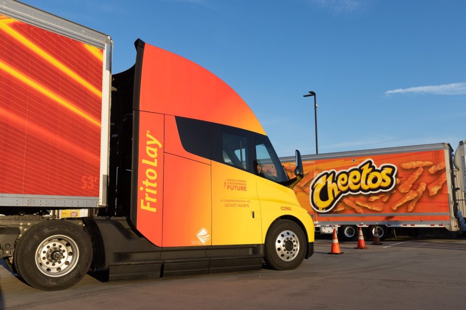 Tesla electric semi truck with bright orange Frito Lay paint scheme, in a parking lot.