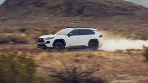 A white 2023 Toyota RAV4 small SUV is driving off-road.