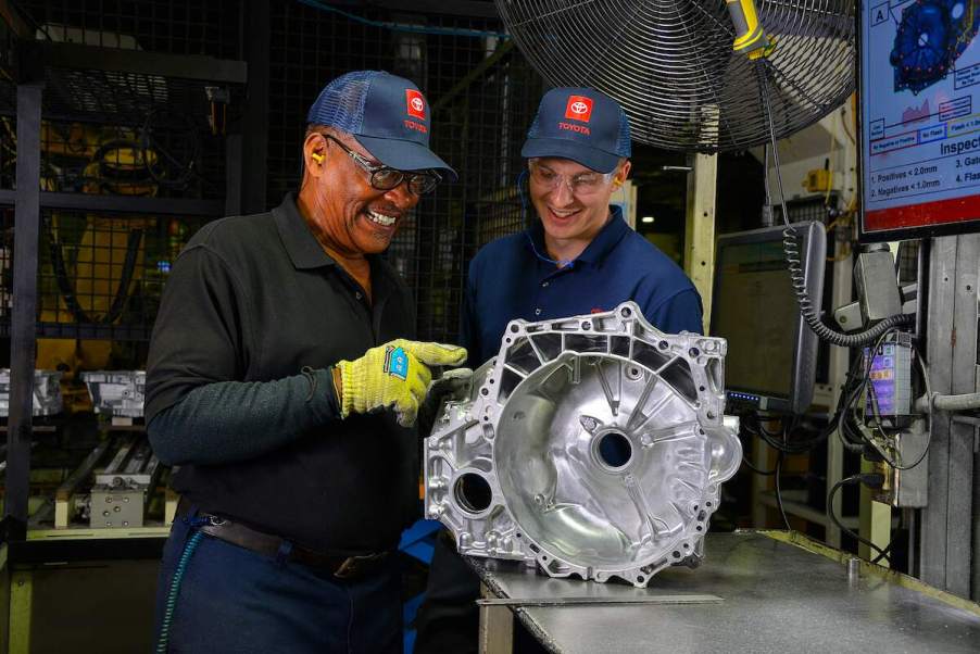 A Toyota Motor North America promo photo of two smiling workers standing over a car part