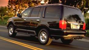 A black 1998 Lincoln Navigator full-size luxury SUV model driving past bushes as the sun sets