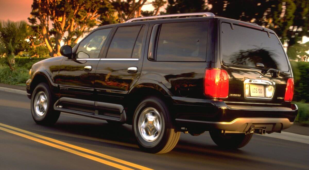 A black 1998 Lincoln Navigator full-size luxury SUV model driving past bushes as the sun sets