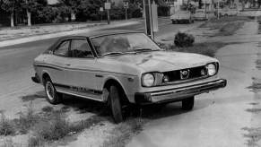 A Loyale predecessor, a Subaru GI Coupe model, parked on the grass and sidewalk