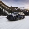 A 2024 Subaru Ascent midsize SUV model with roof rails driving through the snow in a mountain of forests