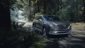 A 2023 Mazda CX-9 midsize SUV model parked on the side of a forest road shadowed by tree branches