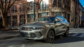 A 2024 Dodge Hornet GT performance-oriented compact SUV model driving through a city past a crosswalk.