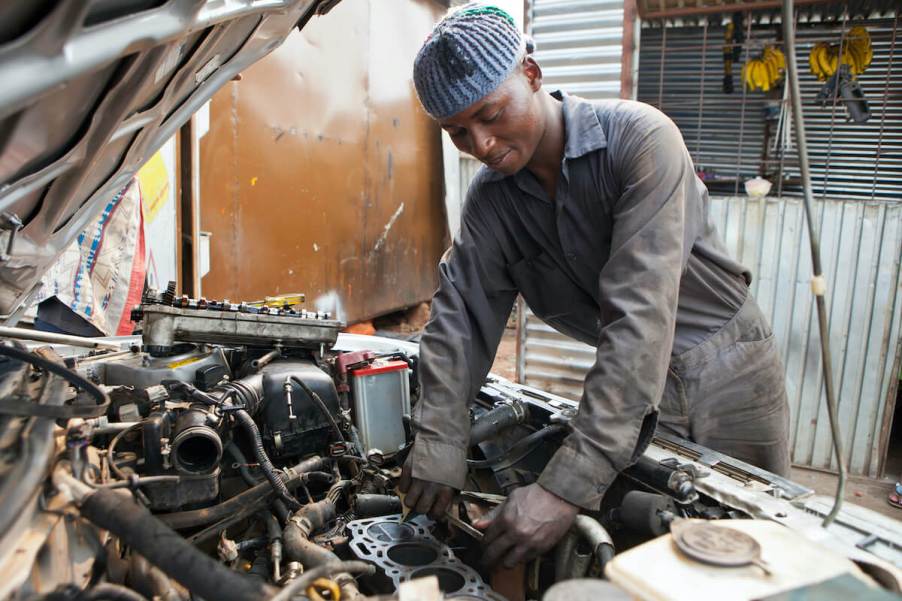 A skilled mechanic leans under the hood of a non-running car, inspecting the engine with a focused expression, tools in hand, as they diagnose and repair the vehicle.