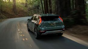 A 2023 Kia Niro compact hybrid SUV model driving on a forest road with its taillights lit up