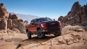 A 2024 GMC Sierra 2500 HD AT4X heavy-duty pickup truck model in Volcanic Red Tintcoat traveling off-road