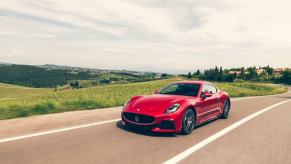 A 2024 Maserati GranTurismo Trofeo grand tourer model driving past farm houses and fields in Italy