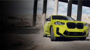 A BMW X4 M compact luxury performance-trimmed SUV model driving through concrete pillars under a bridge