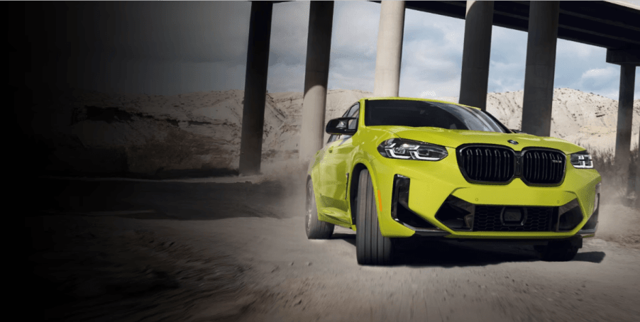 A BMW X4 M compact luxury performance-trimmed SUV model driving through concrete pillars under a bridge