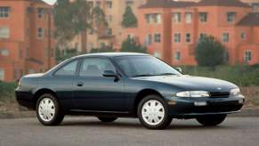 A dark-colored 1996 Nissan 240SX parked in front of orange buildings