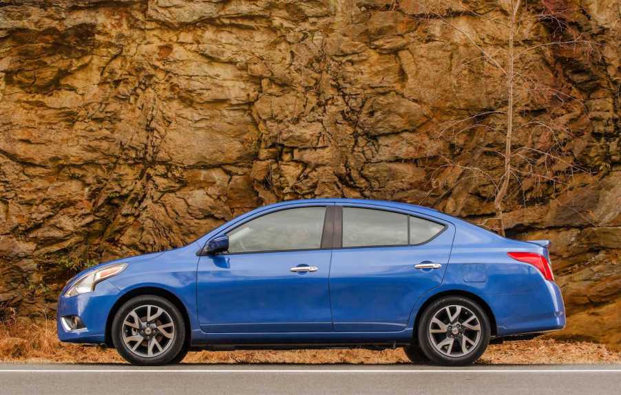 A blue 2016 Nissan Versa compact sedan parked against a rock wall