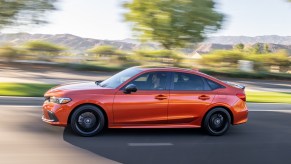 The 2023 Honda Civic Si in orange speeding down a suburban street. It's known for its performance, but the Honda Accord Sport might be a better pick.