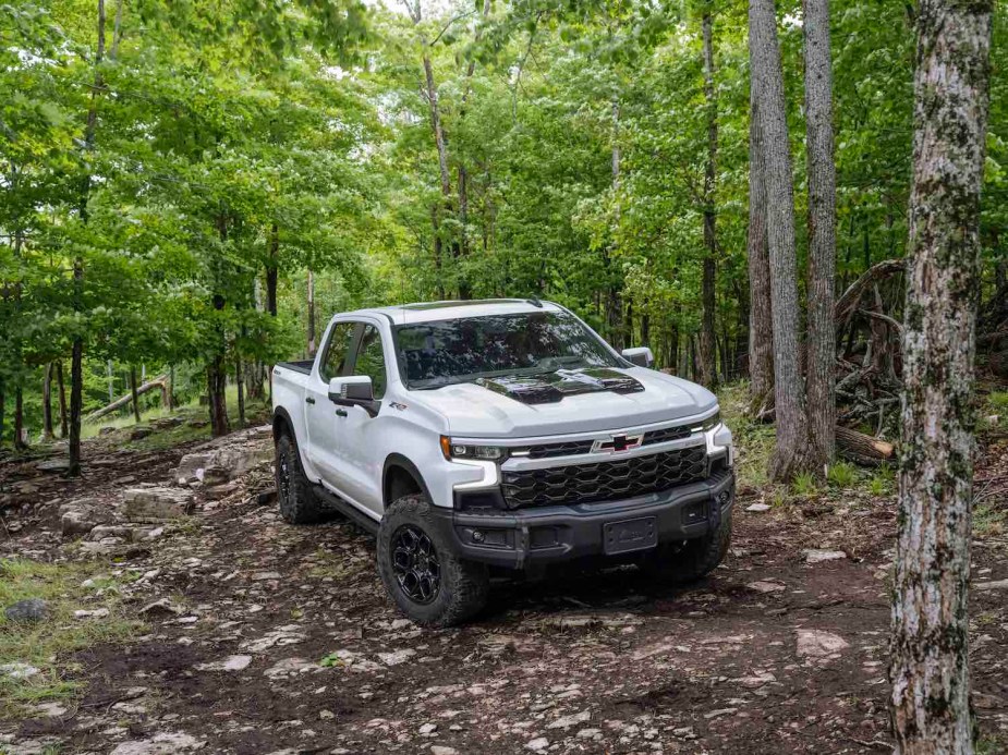 White Silverado 1500 pickup truck on an off-road trail, trees visible in the background.