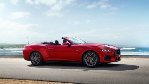 A bright-red 2024 Ford Mustang GT Convertible parks on a road near the beach.