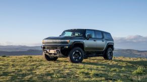 The 2024 GMC Hummer EV SUV all-electric full-size SUV model in Moonshot Green Matte parked on grass