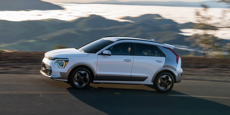 A white Kia Niro EV subcompact electric SUV is driving on the road. 