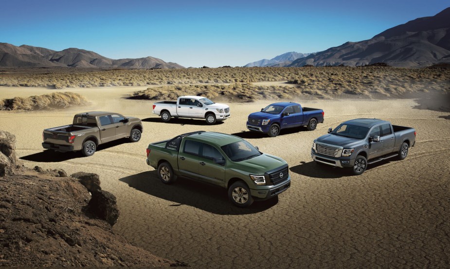 Five Nissan Titan pickup trucks of various trims parked in a desert, a mountain range visible in the background.