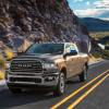 A 2024 Ram 2500 HD Limited Longhorn pickup truck driving on a country highway framed by rocky mountains