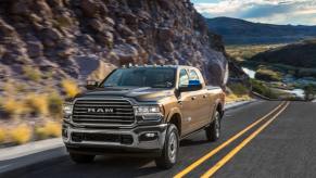 A 2024 Ram 2500 HD Limited Longhorn pickup truck driving on a country highway framed by rocky mountains