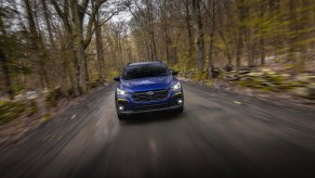 A blue 2024 Subaru Crosstrek driving down a forest road. Compare the 2024 Subaru Crosstrek vs. 2024 Jeep Compass.