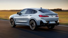 The BMW X4, the most satisfying compact luxury SUV, in gray driving down an empty road.