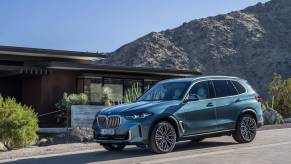 A blue BMW X5 driving down a hill with mountains behind. The X5 and 8 Series are holding back BMW sales this year.