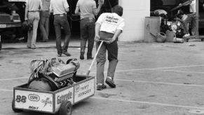 Black and white photo of a crew member pulling an old NASCAR V8 engine in a cart.