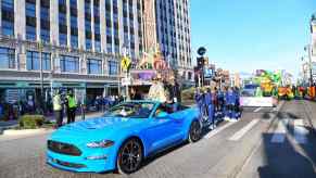 A bright blue Mustang leads a thanksgiving parade down Detroit Michigan's Woodward Avenue.