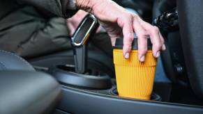 A person with a cup of coffee in their car to drink.