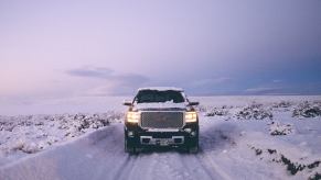 Black GMC Sierra 1500 pickup truck drives down a snowy road.